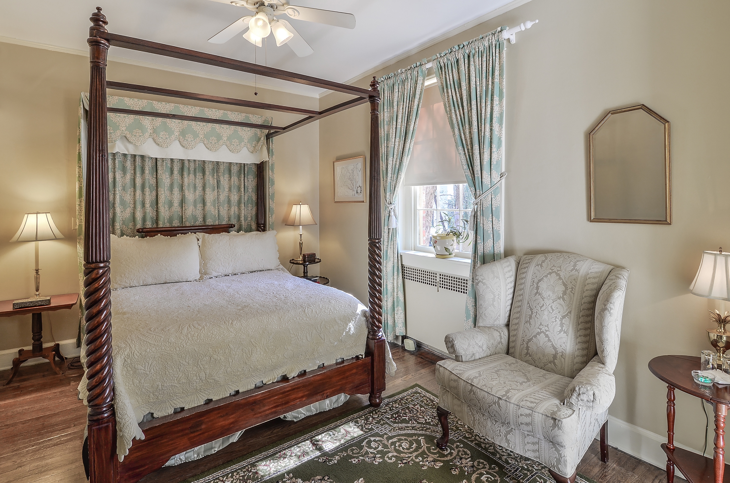 Bedroom in tranquil shades of blue, cream, and white with four-poster bed, cozy armchair, and ceiling fan