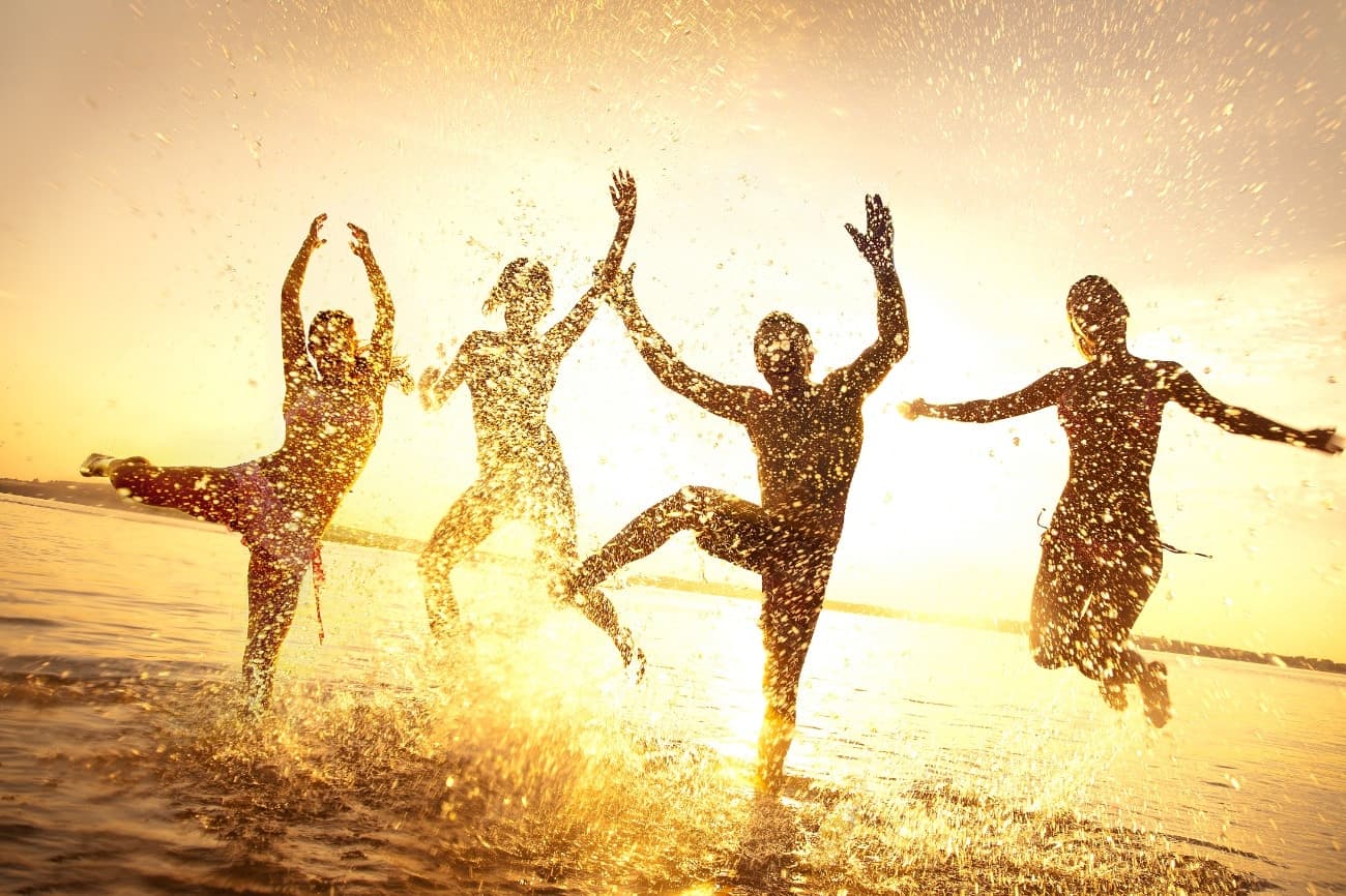 golden backlit silhouettes of people splashing in shallow water