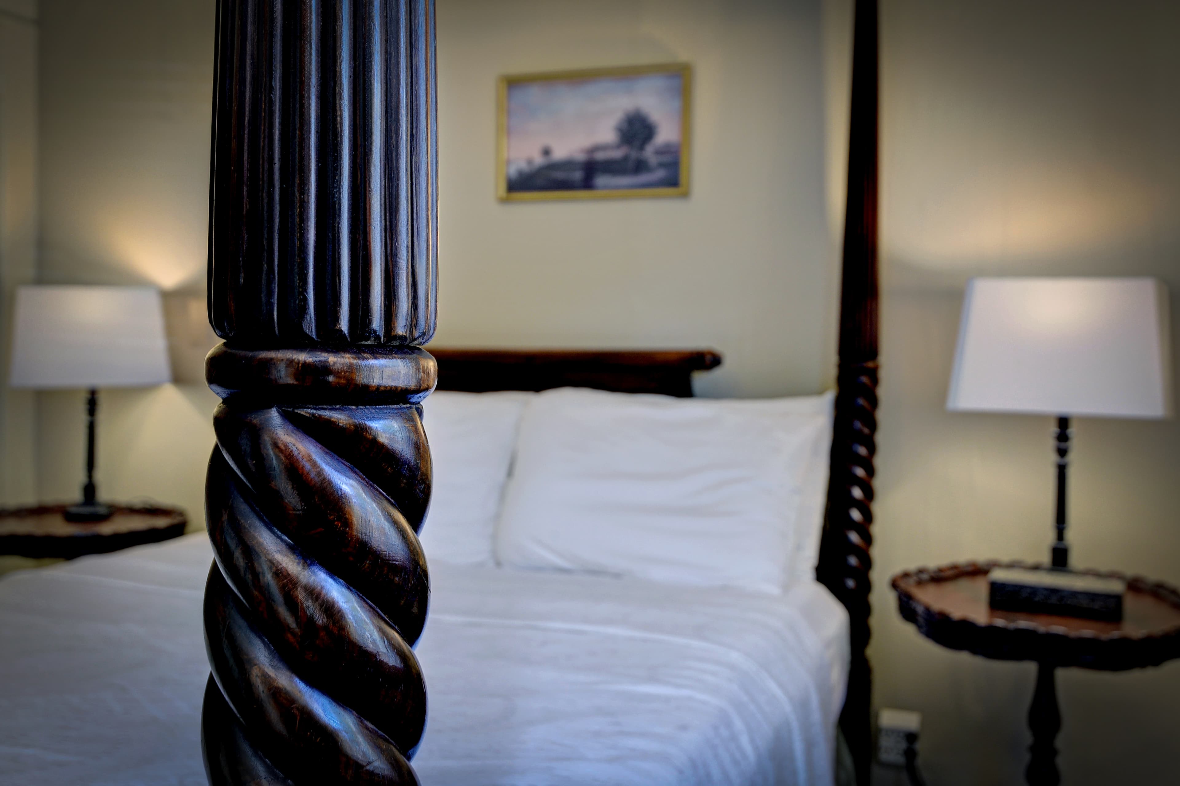 Bedroom with four-poster bed, cozy armchair, and ceiling fan and open door to the bathroom with black and white tile