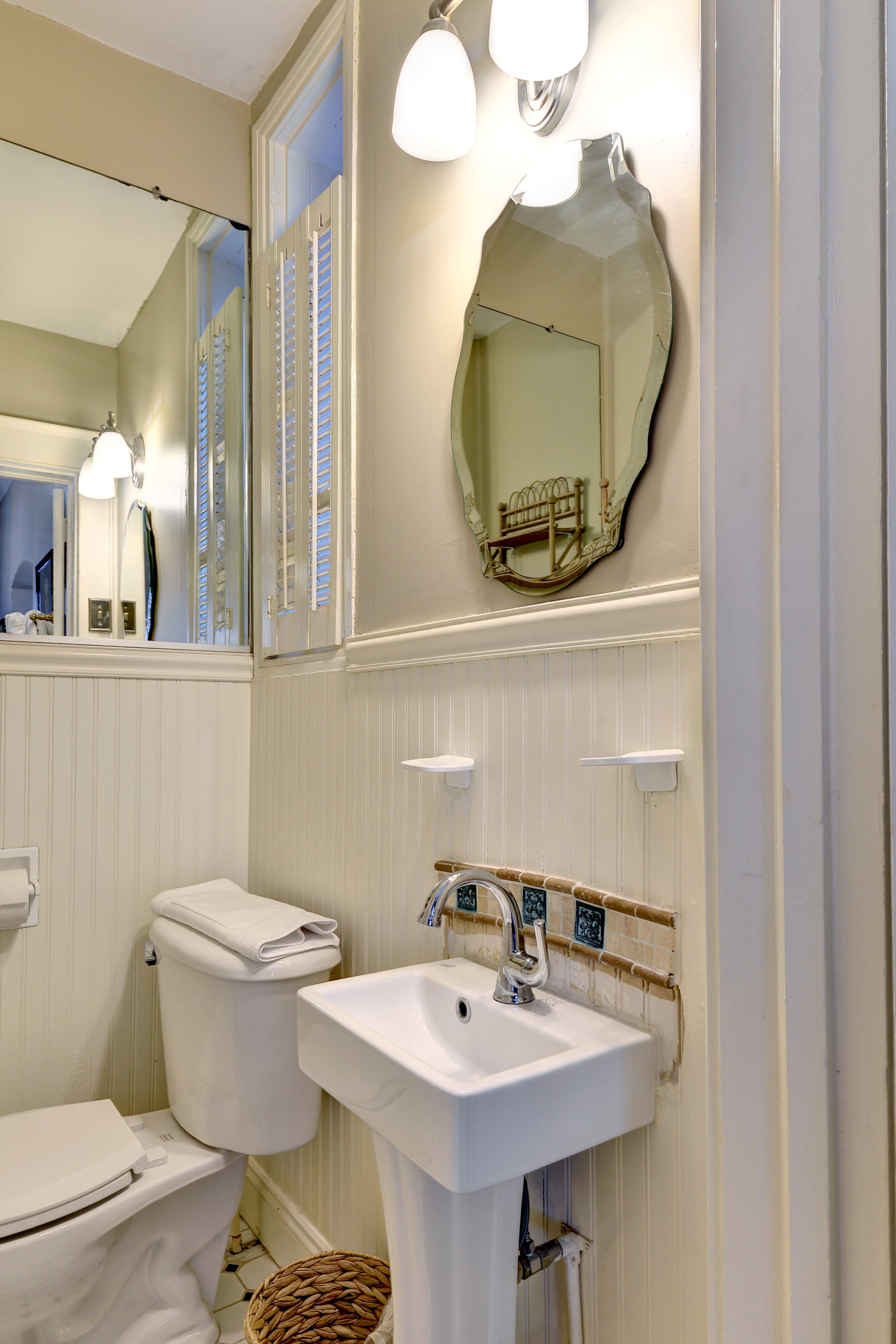 Bathroom with small black and white tile pattern, pedestal sink with decorative scalloped edge, white wainscoting and green walls