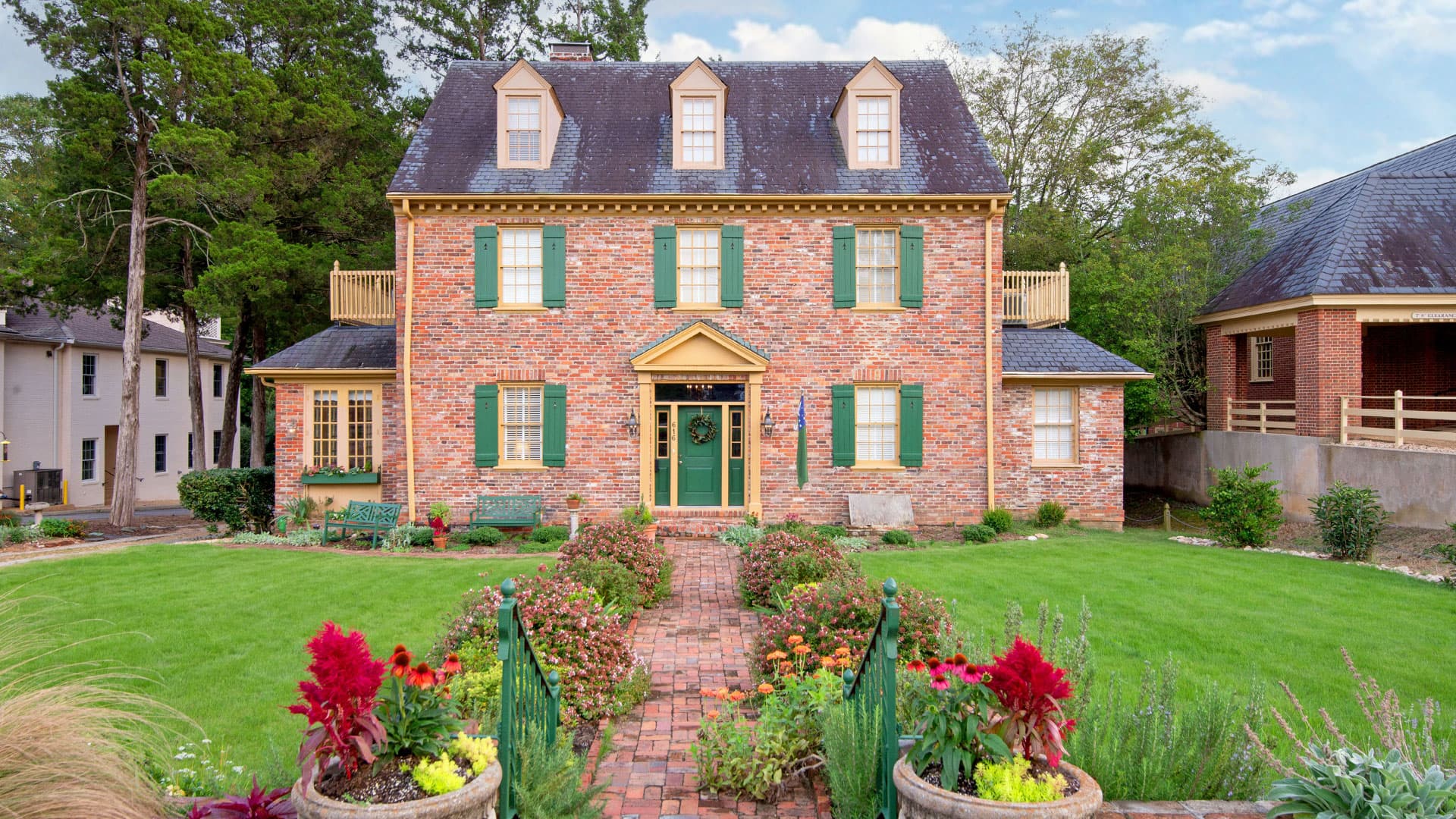 Red brick exterior of cedars bed and breakfast with shutters and dormers with green yard
