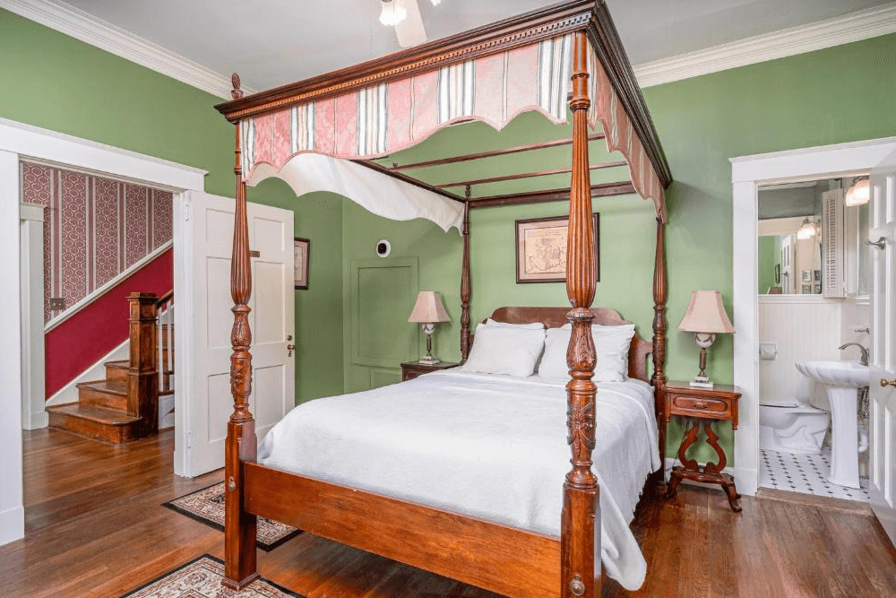 Four poster wood bed with white coverlet, green walls and striped green tapestry hanging from canopy