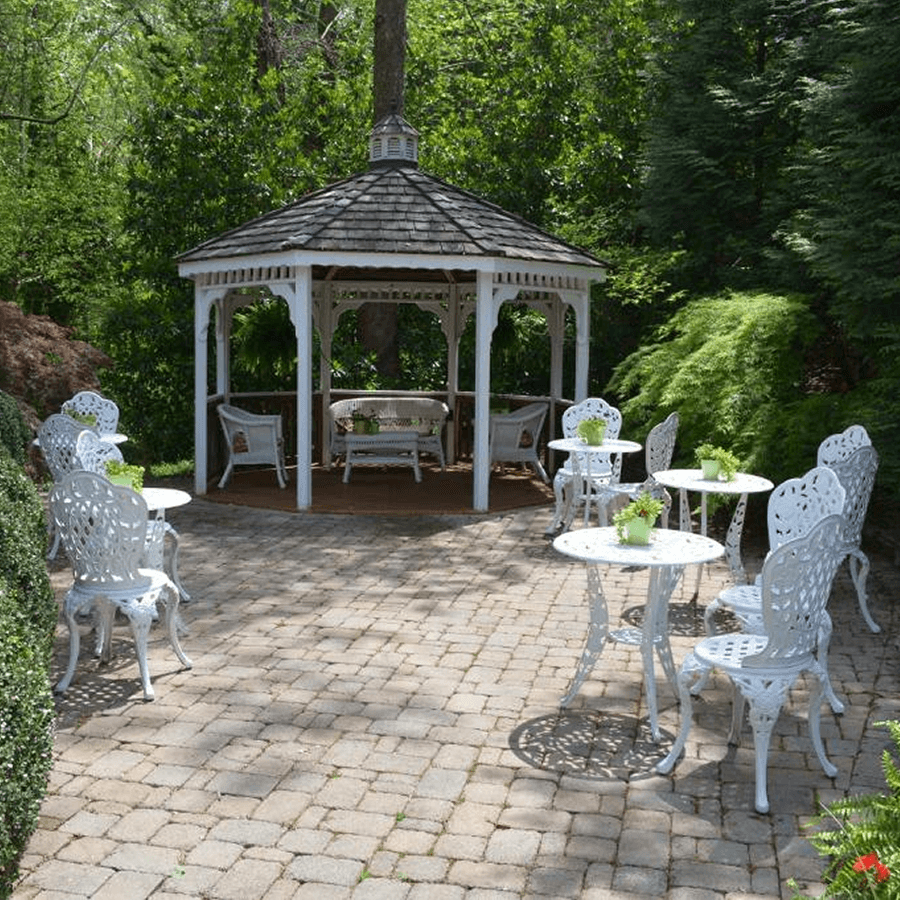 White gazebo set in garden area with brick pathway and white iron garden tables and chairs